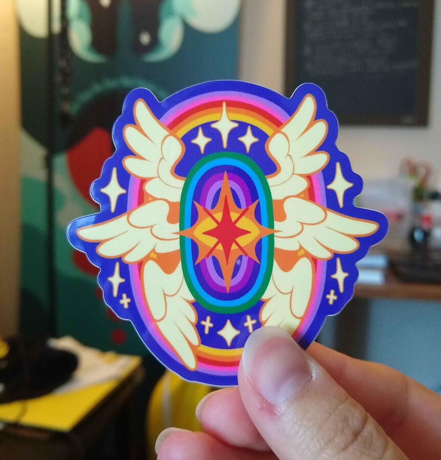 Sticker design of a sparkly seraph with a single eye, six wings and rainbow halos, colors are that of the Gilbert Baker pride flag.