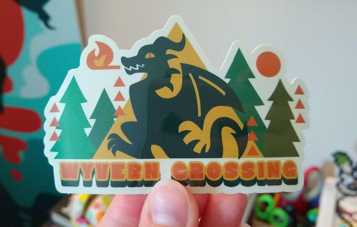 Sticker design of a wyvern silhouette breathing fire, with a fiery pine forest behind. Text reads "Wyvern Crossing".